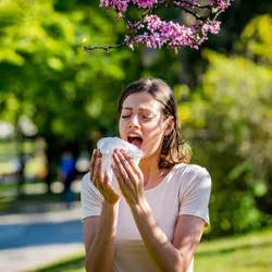 A woman sneezes into a tissue against a natural background
