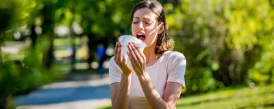 A woman sneezes into a tissue against a natural background
