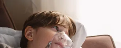 A child lies on their side on a sofa with a breathing apparatus covering their nose and mouth. Such equipment is commonly used for patients who suffer from cystic fibrosis, a once deadly disease that now has become manageable thanks to the triple combination drug Trikafta. Three researchers recently received this year’s Lasker award for their contribution to the development of this drug.