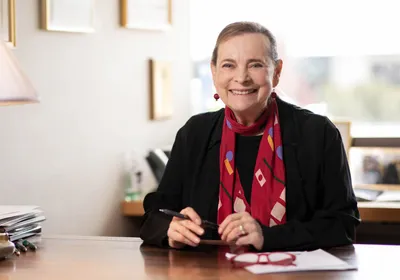 A photograph of developmental biologist Lucy Shapiro, who helped establish the field of systems biology, wearing a black top and red scarf.