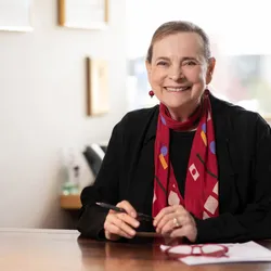 A photograph of developmental biologist Lucy Shapiro, who helped establish the field of systems biology, wearing a black top and red scarf. A photograph of developmental biologist Lucy Shapiro, who helped establish the field of systems biology, wearing a black top and red scarf.