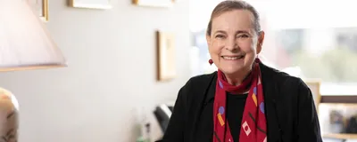 A photograph of developmental biologist Lucy Shapiro, who helped establish the field of systems biology, wearing a black top and red scarf.