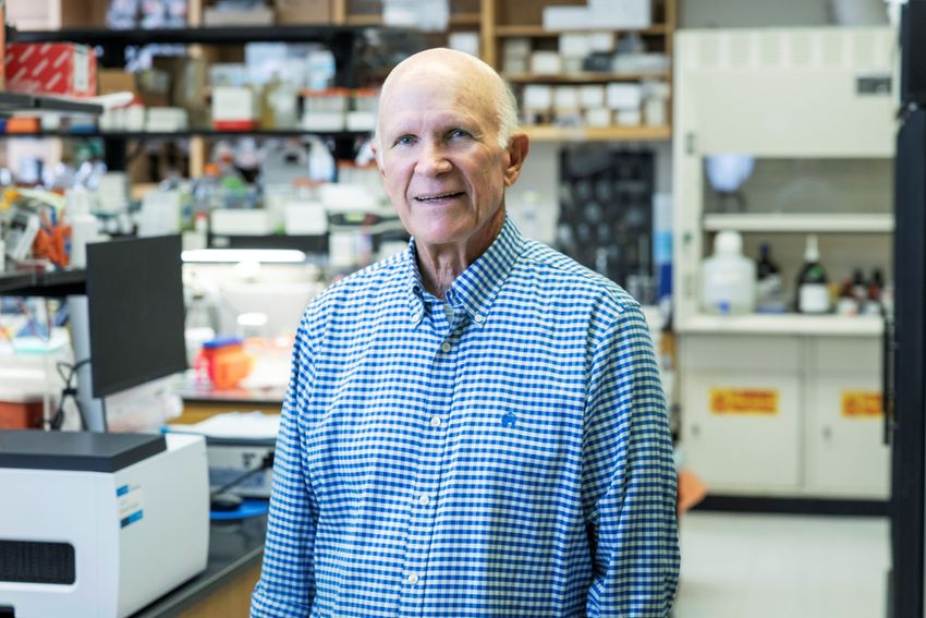 Photograph of Steven McKnight, a molecular biologist at the University of Texas Southwestern Medical Center. He is wearing a blue and white checkered, collared shirt and is standing in a laboratory, with the background blurred.