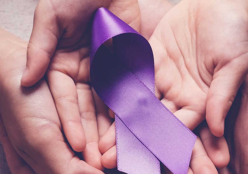 Human hands holding a purple ribbon for pancreatic cancer awareness