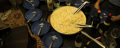 A big bowl of cacio e pepe sits in the center of a table surrounded by empty pasta bowls waiting to be filled.