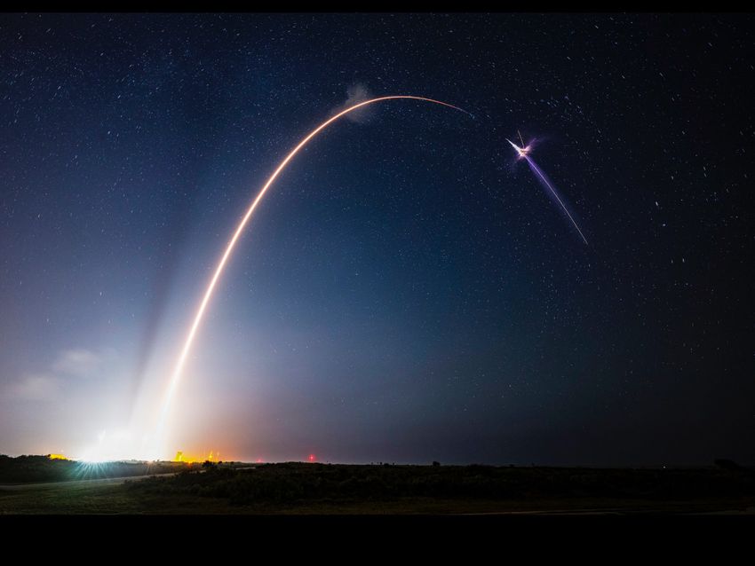 Image of a rocket launch into the night sky. There is an arc of light across a deep blue-sky backdrop.