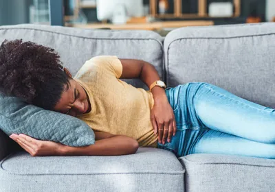 Young woman clutching abdomen in discomfort, showing symptoms of inflammatory bowel disease.