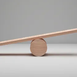 A photo of an unbalanced wooden plank resting on a round wooden ball against a neutral gray background.