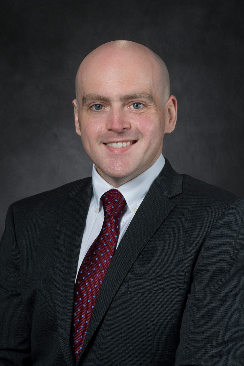 Photograph of Andrew Shepherd, a neuroimmunologist at the University of Texas MD Anderson Cancer Center. Shepherd is wearing a white collared shirt with a dark red tie under a black suit jacket.