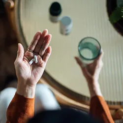 A woman holds two white pills in her left hand and a glass of water in her right. A woman holds two white pills in her left hand and a glass of water in her right.