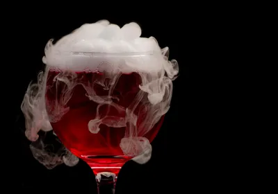 White smoke rises out of a glass of red wine, signifying the ashy taste in wines made from smoke-exposed grapes, also known as smoke taint. 