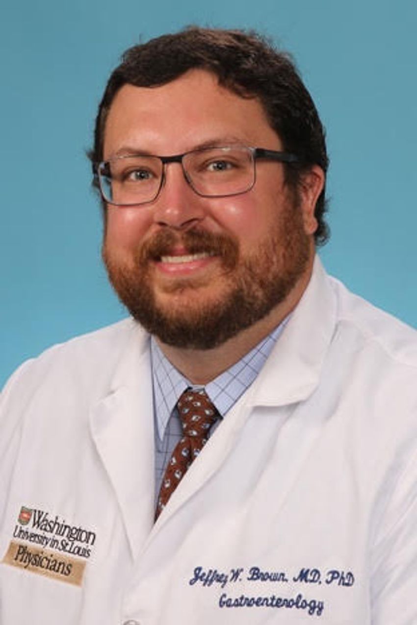 Jeffrey Brown poses in front of a light blue background. He’s wearing glasses and a light checkered shirt with a brownish red patterned tie under a white lab coat, embroidered with his name and credentials (“Jeffrey Brown MD PhD”, “Gastroenterology”) as well as affiliation (“Washington University in St. Louis Physicians”). Jeffrey Brown poses in front of a light blue background. He’s wearing glasses and a light checkered shirt with a brownish red patterned tie under a white lab coat, embroidered with his name and credentials (“Jeffrey Brown MD PhD”, “Gastroenterology”) as well as affiliation (“Washington University in St. Louis Physicians”).