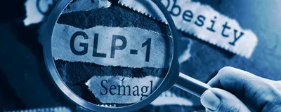 A hand holds a magnifying glass over a strip of paper that says ‘GLP-1’. Surrounding strips of paper have words such as ‘weight loss’, ‘semaglutide’, and ‘obesity’. A hand holds a magnifying glass over a strip of paper that says ‘GLP-1’. Surrounding strips of paper have words such as ‘weight loss’, ‘semaglutide’, and ‘obesity’.