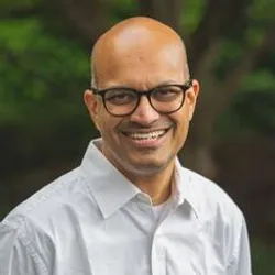 Santhosh Girirajan wears glasses and a light-colored shirt in a headshot taken outside. Santhosh Girirajan wears glasses and a light-colored shirt in a headshot taken outside.