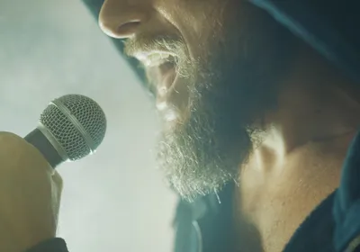 Photograph of the bottom half of a man’s face while he sings into a microphone. 