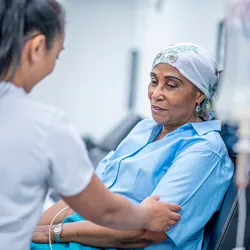 A healthcare professional touches the arm of a seated patient who is undergoing cancer treatment. A healthcare professional touches the arm of a seated patient who is undergoing cancer treatment.