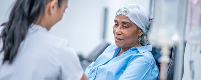 A healthcare professional touches the arm of a seated patient who is undergoing cancer treatment. A healthcare professional touches the arm of a seated patient who is undergoing cancer treatment.