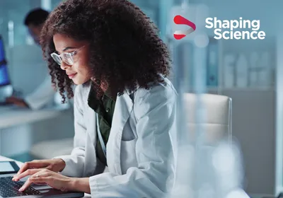 A scientist in a white lab coat types on her computer within a life science research lab. A scientist in a white lab coat types on her computer within a life science research lab.