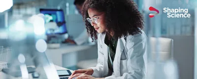 A scientist in a white lab coat types on her computer within a life science research lab.