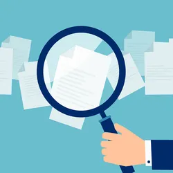 A magnifying glass held against paper illustrates the academic peer review process.