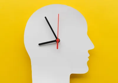 Depiction of circadian rhythm with clock hands on top of a white cutout of a human head on a yellow background. 