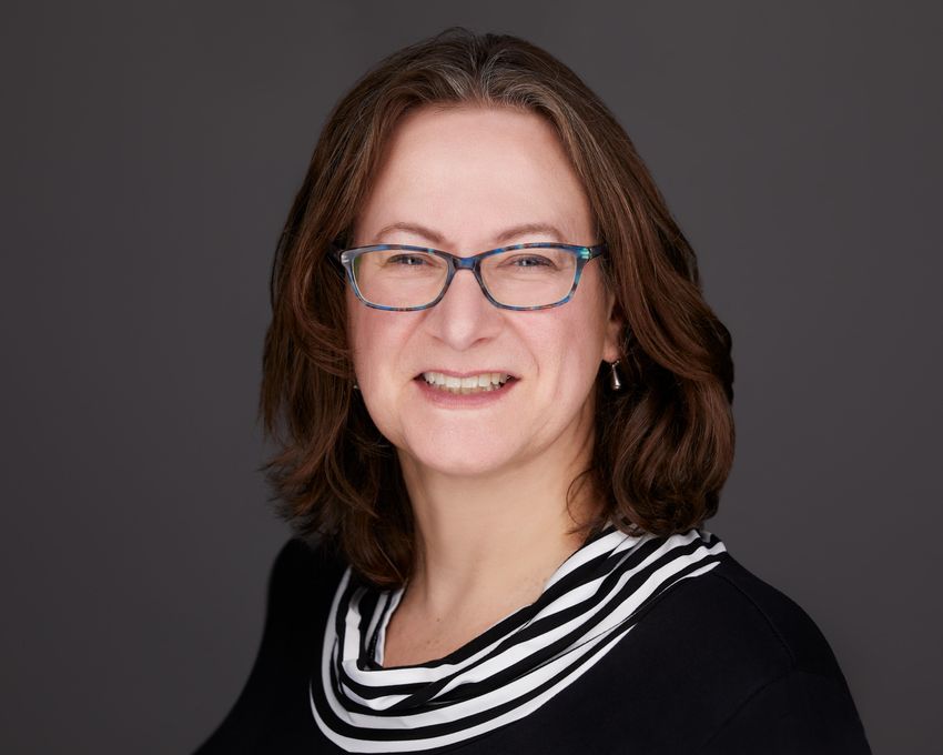 Elisabeth Bik poses in front of a grey background. She’s wearing a black top with black and white stripes around the collar, glasses, and earrings. Elisabeth Bik poses in front of a grey background. She’s wearing a black top with black and white stripes around the collar, glasses, and earrings.