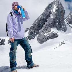 A mountain climber stands in front of snowy mountains and holds a blue canister of portable supplemental oxygen to his face to relieve symptoms of hypoxia due to the high altitude.