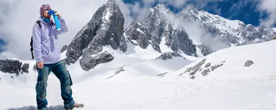 A mountain climber stands in front of snowy mountains and holds a blue canister of portable supplemental oxygen to his face to relieve symptoms of hypoxia due to the high altitude. A mountain climber stands in front of snowy mountains and holds a blue canister of portable supplemental oxygen to his face to relieve symptoms of hypoxia due to the high altitude.