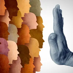 Representative image of travel bans. One the left are silhouettes of human faces in colors ranging from cream to tan to brown. A hand extending from the right is held up in a “stop” signal in front of them in the middle of the image. 