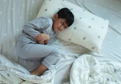 Boy lying in bed with a stomachache, signifying gastroenteritis caused due to human astroviruses.