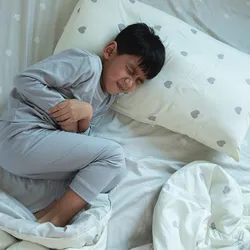 Boy lying in bed with a stomachache, signifying gastroenteritis caused due to human astroviruses.