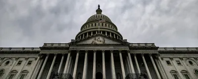 The US capitol building is shown from below at an angle, with a cloudy sky in the background. The US capitol building is shown from below at an angle, with a cloudy sky in the background.