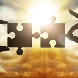 Hands collect gear in a puzzle against the sky in the sunset, representing academia-industry partnership.