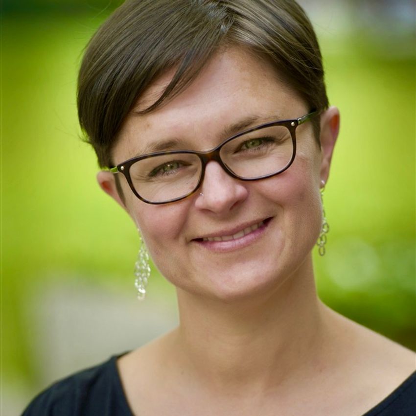 Kate Shoveller, a nutritional physiologist at the University of Guelph, smiles at the camera. She has short dark hair and is wearing square-framed glasses, long earrings, and a black shirt.