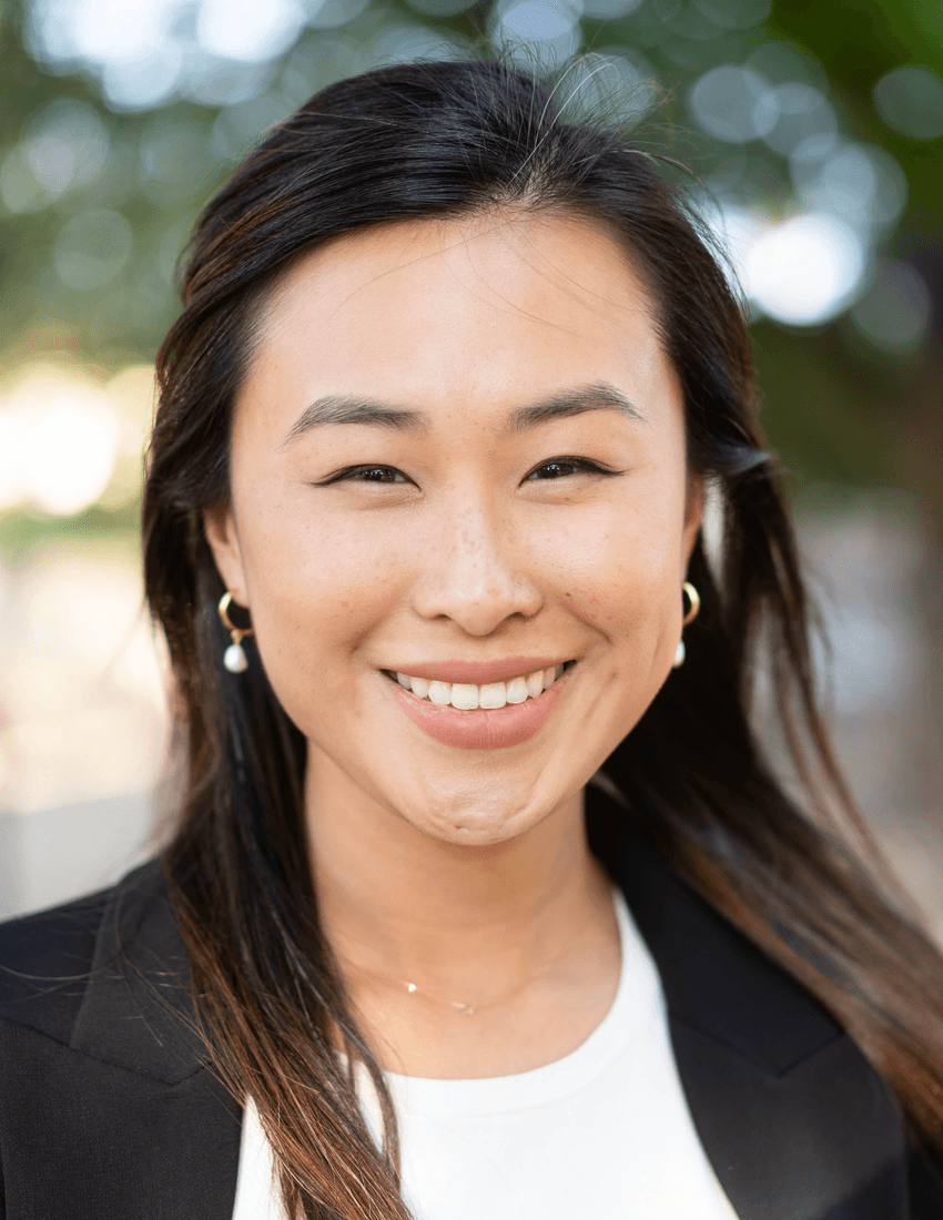 Shirley Jiang has long, dark hair and is wearing a white shirt and black jacket, smiling at the camera.