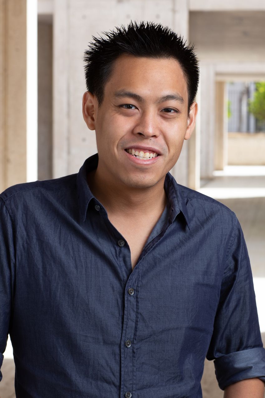 Image of postdoctoral researcher Travis Lee. He smiles at the camera and is wearing a dark blue button up shirt.