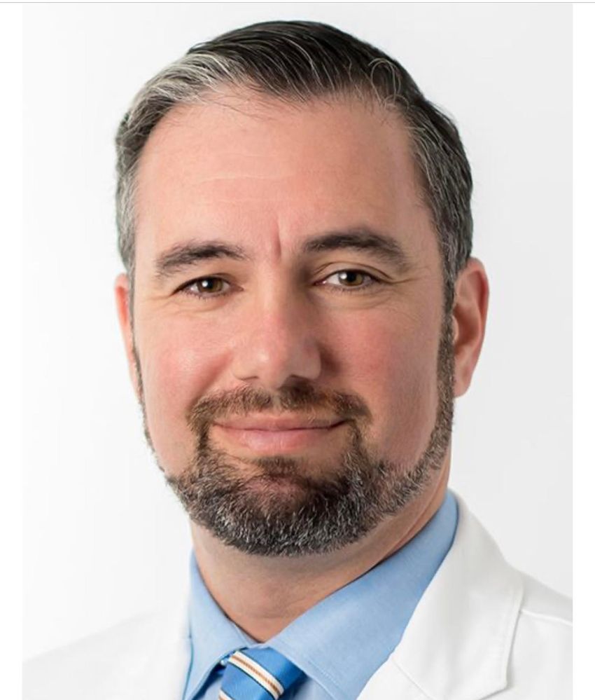 A photo of Ari Green, who studies multiple sclerosis, in a blue shirt and white coat.