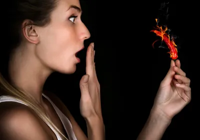Person looks shocked, holding red chili pepper on fire. Some people like spicy food more than others. 