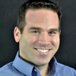 Joshua Selsby wears a blue shirt and smiles in a headshot.