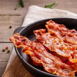 Hot fried crispy bacon slices in skillet on wooden background. Fat-associated sensory cues such as bacon odors in maternal diet may influence offsprings’ predisposition to obesity during adulthood. 