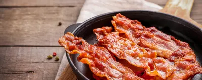 Hot fried crispy bacon slices in skillet on wooden background. Fat-associated sensory cues such as bacon odors in maternal diet may influence offsprings’ predisposition to obesity during adulthood. 