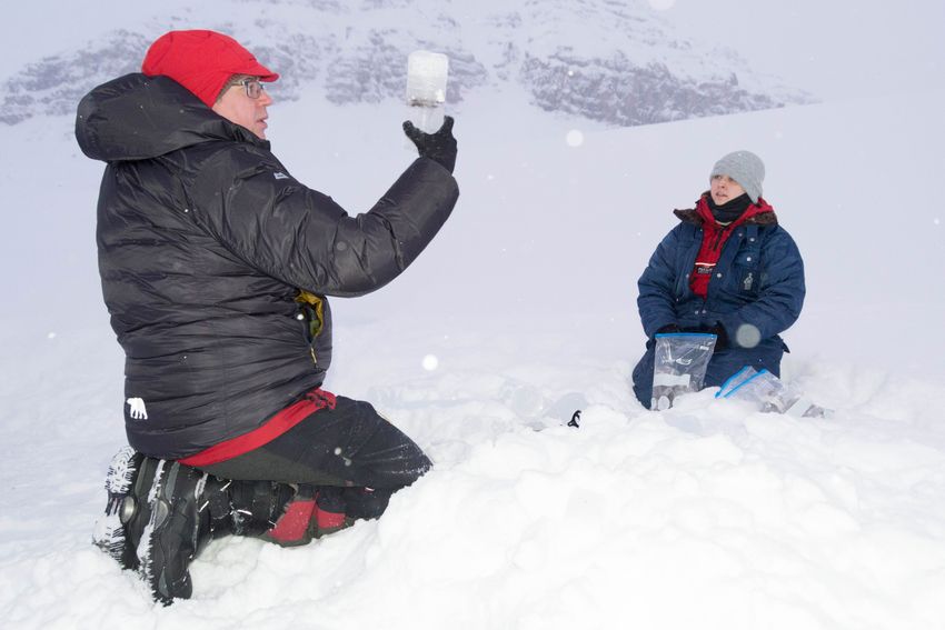 Arwyn Edwards holds an ice core containing a frozen cryoconite hole in the late polar night. One of his team members sits on the ice across from him.