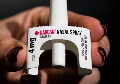 A hand holds naloxone nasal spray.
