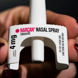 A hand holds naloxone nasal spray.
