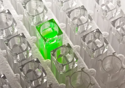 Cuvettes with clear colorless liquid surrounding one cuvette with bright green luminescing liquid Cuvettes with clear colorless liquid surrounding one cuvette with bright green luminescing liquid