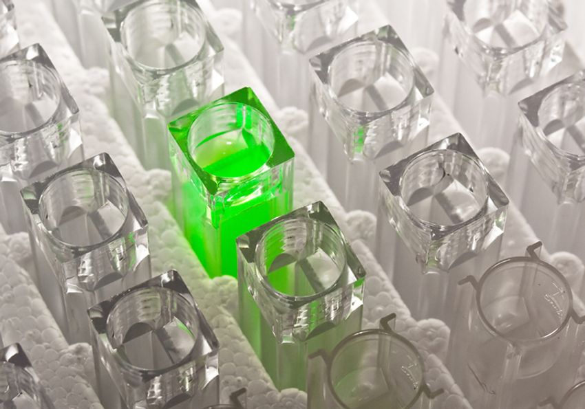 Cuvettes with clear colorless liquid surrounding one cuvette with bright green luminescing liquid Cuvettes with clear colorless liquid surrounding one cuvette with bright green luminescing liquid