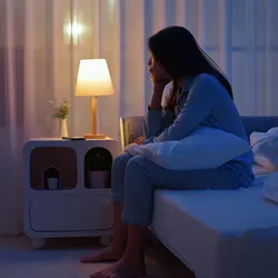 Image of a young woman sitting alone by the bedside. She appears troubled and unable to sleep.