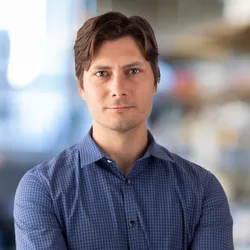 Image of Dmitry Lyumkis. He wears a blue button-up shirt and looks at the camera.