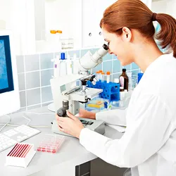A female scientist analyzing samples through a microscope, engaged in histopathology studies in a laboratory environment.