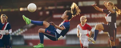 Three female soccer players watch as one of their teammates does a bicycle kick on the soccer pitch.